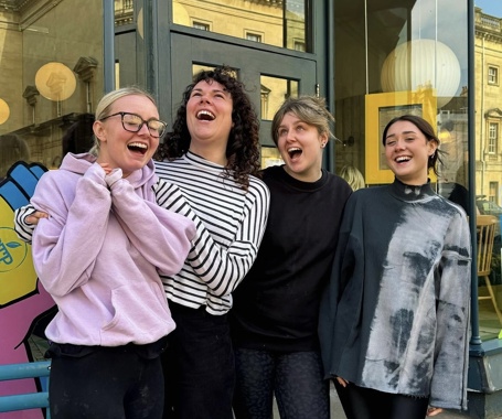 Four women who work for Boston, arms around one another, smiling and laughing